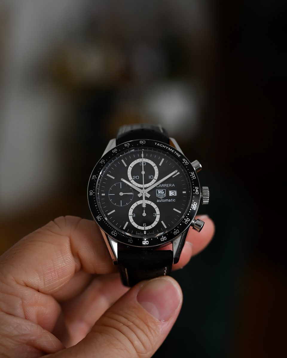Eine Hand hält einen Chronographen mit schwarzem Zifferblatt